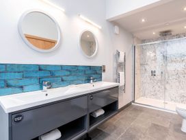 A bathroom with double sinks blue tile backsplash two round mirrors a glass shower and a towel rack at Blackwood Forest Golden Oak Hideaway in Blackwood Forest