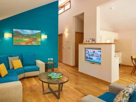 A living room with blue and beige sofas a wooden coffee table with a Scrabble game a wall-mounted TV and a turquoise accent wall with a landscape painting at Beddgelert Golden Oak - freshly inspired design in Beddgelert Eryri Snowdonia