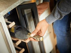 A person placing a bottle of wine in a wine cooler in a kitchen at Beddgelert Golden Oak - freshly inspired design Beddgelert Eryri Snowdonia