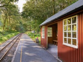 A small train station platform with a red wooden shelter and railway tracks through a forest at Beddgelert Golden Oak - freshly inspired design Beddgelert Eryri Snowdonia