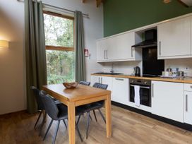 A kitchen with white cabinets wooden table and black chairs near a large window with green curtains at Keldy Classic Golden Oak in Keldy Forest