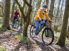 Two women wearing helmets cycling on a forest trail surrounded by trees and fallen leaves at Keldy Classic Golden Oak in Keldy Forest