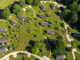 An aerial view of a grassy area with multiple small cabins and winding paths surrounded by trees at Forest of Dean Meadow - Golden Oak in Forest Of Dean