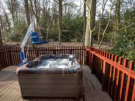 A wooden deck with a hot tub and a blue chair lift surrounded by trees at Glentress Forest Silver Birch wheelchair accessible cabin in Peebles