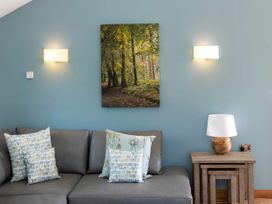 A gray sofa with patterned pillows under a wall painting of a forest next to nested wooden tables with a lamp at Glentress Forest Silver Birch wheelchair accessible cabin in Peebles