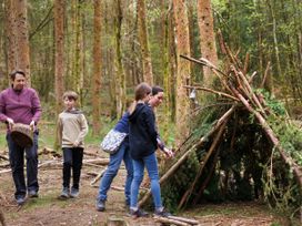 Four people building a shelter with sticks and branches in a forest at Ardgartan Argyll Golden Oak in Ardgartan Loch Long