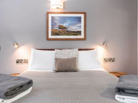 A bed with gray quilted bedding and pillows under a landscape picture and wall lamps at Glentress Forest White Willow Premium in Glentress Forest Peebles