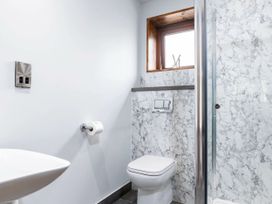 A bathroom with a toilet, sink, toilet paper holder, small window, and a glass shower door at Glentress Forest White Willow Premium in Glentress Forest Peebles