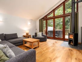 A living room with gray sofas wooden coffee table wood burning stove and large glass doors overlooking trees at Glentress Forest Golden Oak Valley View Glentress Forest Peebles