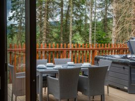 An outdoor deck with a dining table, six chairs, a hot tub, and a wooden railing with trees in the background at Glentress Forest Golden Oak Valley View Glentress Forest, Peebles