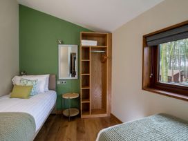 A bedroom with two single beds a wooden open closet and a window overlooking trees at Garwnant Golden Oak Treehouse Garwnant Bannau Brycheiniog Brecon Beacons