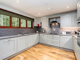 A kitchen with white cabinets a wooden floor and a large window showing trees at Glentress Forest Golden Oak in Glentress Forest Peebles