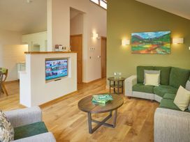A living room with green and beige sofas a wooden coffee table with a Scrabble board game and a TV built into a partial wall at Beddgelert Silver Birch - freshly inspired design Beddgelert Eryri Snowdonia