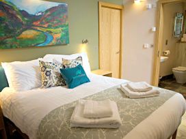 A bedroom with a double bed with pillows and towels next to a door and an open bathroom door at Beddgelert Silver Birch - freshly inspired design in Beddgelert Eryri Snowdonia