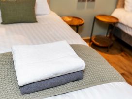 A folded white towel and a folded gray towel on a bed with a textured green throw in a bedroom with bedside tables at Ardgartan Argyll Golden Oak Lochside Ardgartan Loch Long