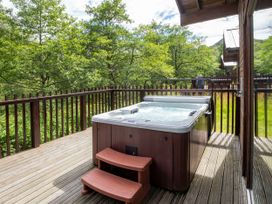 An outdoor wooden deck with a hot tub and steps surrounded by trees at Strathyre Classic Golden Oak in Strathyre Ben Ledi