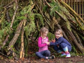 Two children playing inside a shelter made of branches and leaves in a forest