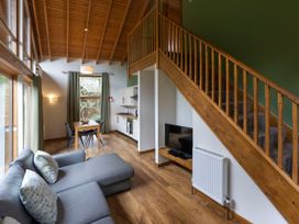 A living room with a grey sofa a wooden dining table four chairs a wall-mounted television under wooden stairs and kitchen area at Deerpark Classic Silver Birch in Deerpark Forest