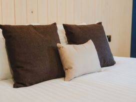A bed with two dark brown pillows and one smaller beige pillow at Glentress The Unfurl Treehouse in Glentress Forest Peebles
