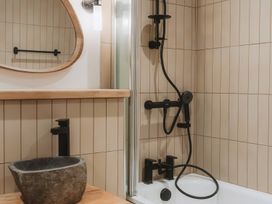 A bathroom with a stone sink wooden countertop a mirror and a bathtub with a black shower system at Glentress The Unfurl Treehouse in Glentress Forest Peebles