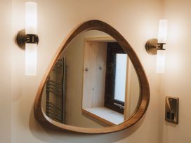 A bathroom mirror with wooden frame reflecting a window and radiator between two wall sconces at Glentress The Unfurl Treehouse in Glentress Forest Peebles