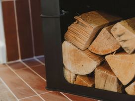 A stack of firewood inside a black metal firewood holder on a tiled floor at Glentress The Unfurl Treehouse Glentress Forest Peebles