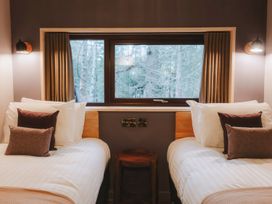 A bedroom with two beds separated by a small wooden stool under a window with curtains at Glentress The Unfurl Treehouse Glentress Forest Peebles