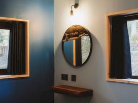 A room corner with two windows with black curtains a round mirror above a wooden shelf and a wall light at Glentress The Unfurl Treehouse Glentress Forest Peebles