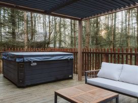 An outdoor wooden deck with a covered hot tub a cushioned sofa and a wooden table at Glentress The Unfurl Treehouse Glentress Forest Peebles