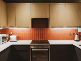 A kitchen with wooden cabinets orange tiled backsplash microwave toaster electric kettle and oven at Glentress The Unfurl Treehouse Glentress Forest Peebles