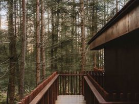 A wooden balcony with railings attached to a building in a forest with tall trees at Glentress The Unfurl Treehouse Glentress Forest Peebles
