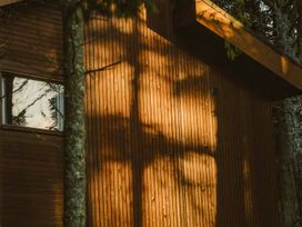 Wooden exterior wall of a building with shadows of trees and a window reflecting trees at Glentress The Unfurl Treehouse in Glentress Forest Peebles
