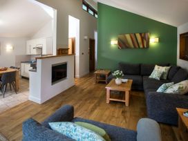A living room with dark gray sofas a green accent wall wooden tables and an open kitchen area at Blackwood Forest Golden Oak Treehouse in Blackwood Forest