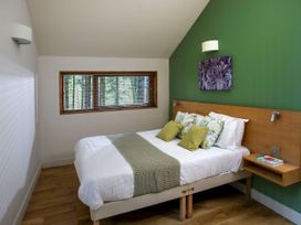 A bedroom with a bed with green and floral pillows by a window at Blackwood Forest Golden Oak Treehouse in Blackwood Forest