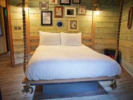A bedroom with a hanging bed white bedding picture frames on wooden walls and a small fireplace at Blackwood Forest Golden Oak Treehouse in Blackwood Forest