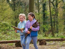 Two children carrying sticks and walking in a forest clearing at Blackwood Forest Golden Oak Treehouse Blackwood Forest