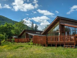 Wooden cabins with large windows and fences in a grassy area with trees and hills in the background at Ardgartan Argyll Silver Birch in Ardgartan Loch Long
