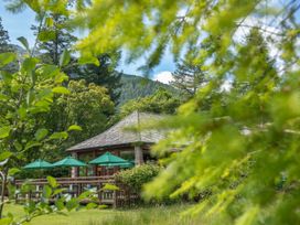An outdoor seating area with green umbrellas surrounded by trees and hills at Ardgartan Argyll Silver Birch in Ardgartan Loch Long
