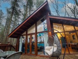 A wooden cabin with large glass windows and doors a glass table with wicker chairs and a hanging wicker chair on a wooden deck at Delamere Forest Golden Oak Hideaway in Delamere Forest