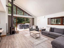 A living room with sofas a coffee table wood stove and large windows opening to a deck with a hot tub at Strathyre White Willow Premium in Strathyre Ben Ledi