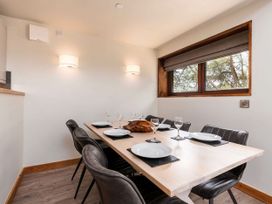 A dining room with a table set for six near a window with trees outside at Strathyre White Willow Premium in Strathyre Ben Ledi