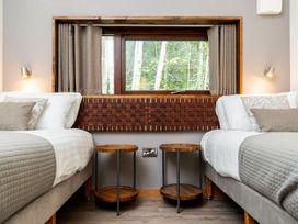 A bedroom with two single beds, wooden side tables, a window with curtains and a view of trees at Strathyre White Willow Premium in Strathyre Ben Ledi