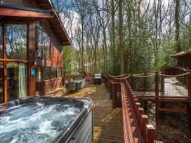 An outdoor wooden deck with a hot tub dining table barbecue grill and forest surroundings at Delamere Forest Golden Oak Treehouse Delamere Forest