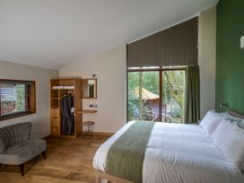 A bedroom with a bed near a large window a gray chair an open wardrobe and a small desk at Delamere Forest Golden Oak Treehouse in Delamere Forest