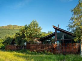 Two wooden houses with glass walls and fences surrounded by trees and grass with hills in the background at Ardgartan Argyll Golden Oak Ardgartan Loch Long