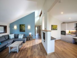 An open plan living area with a gray sectional sofa, wooden coffee table, blue accent wall with wall lights, and a kitchen with white cabinets at Forest of Dean Woodland - Silver Birch wheelchair accessible cabin in Forest Of Dean