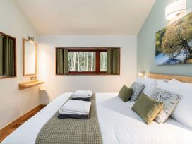 A bedroom with a bed with pillows and folded towels a window with green curtains a mirror and a wooden shelf on the wall at Glentress Forest Golden Oak in Glentress Forest Peebles