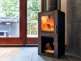 A wood burning stove with fire inside and logs below next to glass doors showing outdoor deck