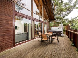 A wooden deck with table and four chairs and a hot tub next to a cabin at Keldy Classic Silver Birch wheelchair accessible cabin in Keldy Forest