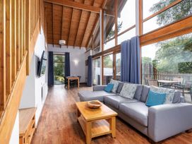 A living room with a gray sofa and wooden coffee table next to large windows with blue curtains at Keldy Classic Silver Birch wheelchair accessible cabin in Keldy Forest